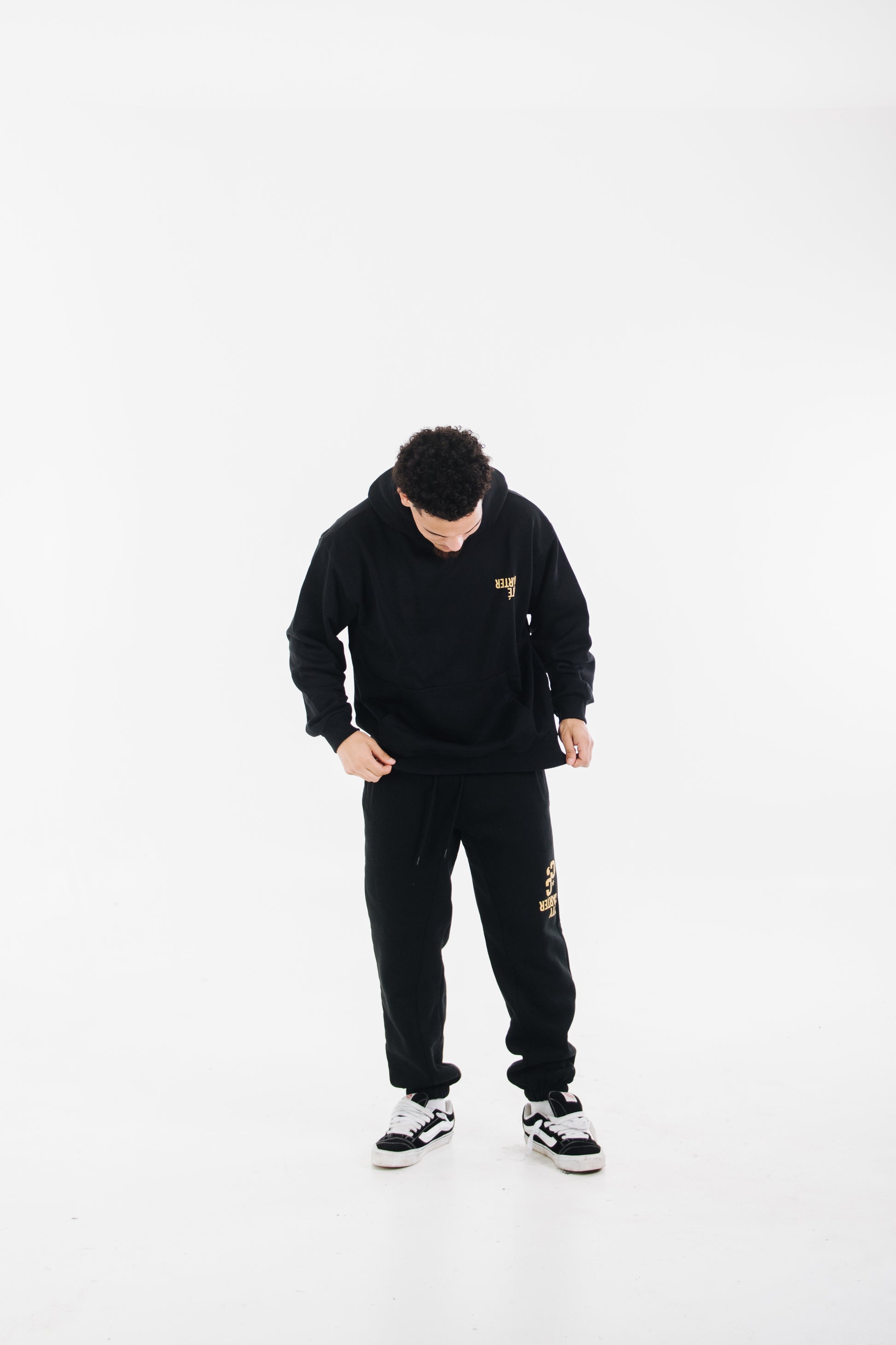 Model wearing black tracksuit with yellow chest logo and printed pants