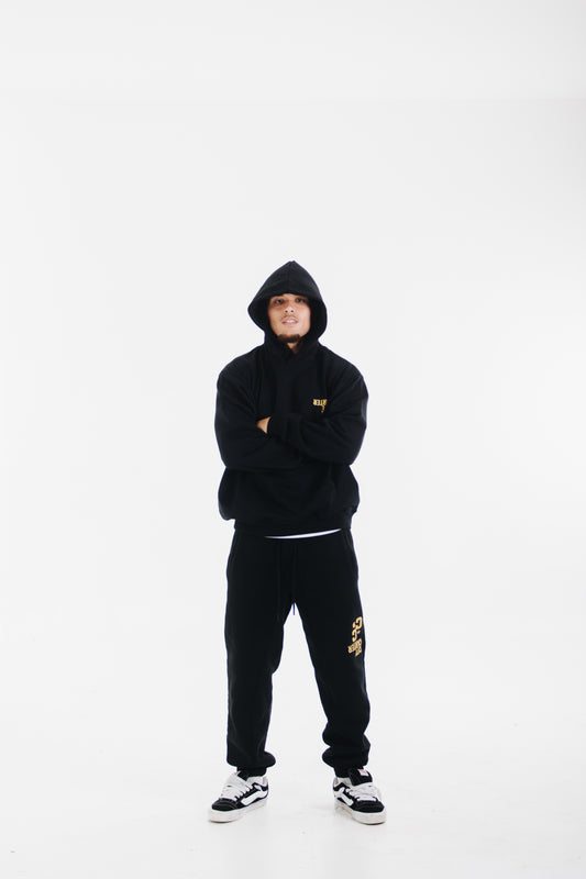 Model wearing black tracksuit with yellow chest logo and printed pants